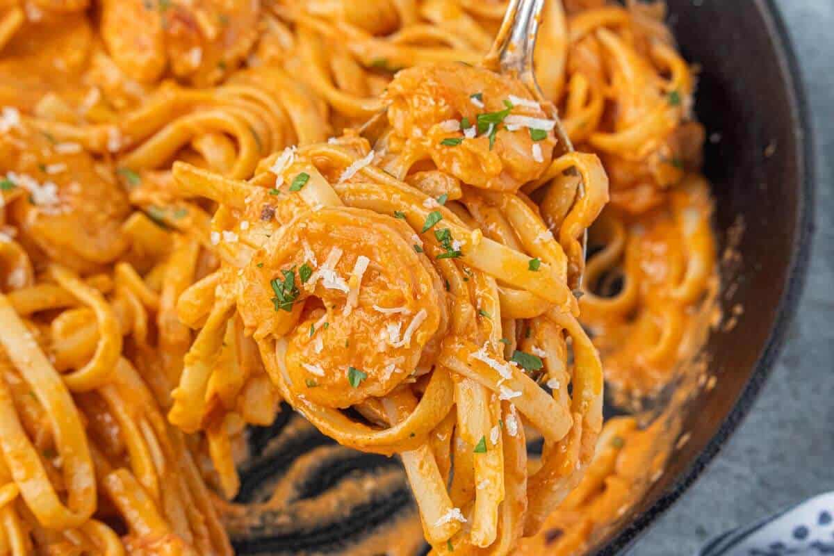 Tender shrimp pasta coated in creamy vodka sauce being lifted from a cast iron skillet.
