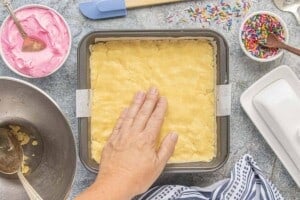 Pressing the sugar cookie bar dough evenly into a parchment-lined 8x8-inch baking pan before baking.
