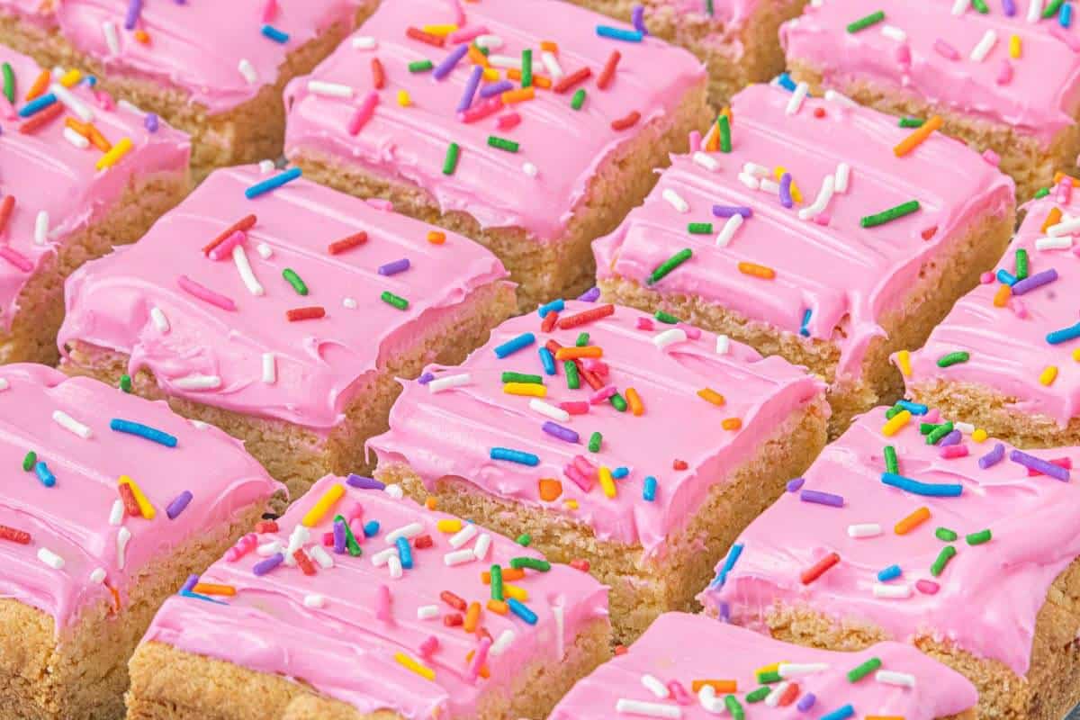 Cake mix Lofthouse sugar cookie bars cut into squares and topped with pink buttercream frosting and rainbow jimmies.