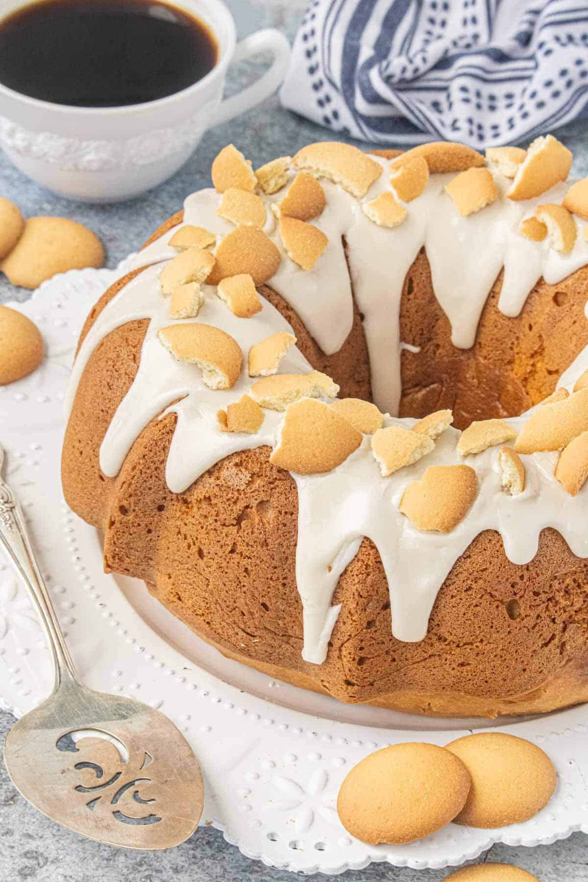 Vanilla Wafer Bundt Cake with vanilla glaze and crushed vanilla wafers on a white cake stand, served with coffee.