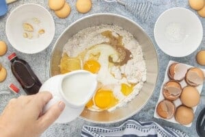 Milk is poured into a mixing bowl with cake mix, crushed vanilla wafers, eggs, oil, pudding mix, and vanilla to make Vanilla Wafer Bundt Cake batter.