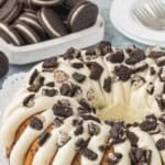 Copycat Oreo Cookies and Cream Bundt Cake topped with thick cream cheese frosting and crushed Oreo cookies, with whole Oreos in the background. With bold print overlay.