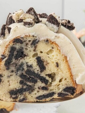 Slice of Oreo Bundt Cake on a cake server showing Oreo cookie pieces baked throughout the cake.