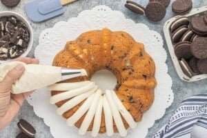 Creamy frosting being piped over the top of the cooled Oreo Bundt Cake.