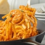 Close-up of creamy pink shrimp pasta with fettuccine, Parmesan cheese, and fresh parsley lifted from a skillet.