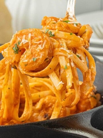 Close-up of creamy pink shrimp pasta with fettuccine, Parmesan cheese, and fresh parsley lifted from a skillet.
