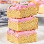 Stack of three cake mix Lofthouse sugar cookie bars topped with pink buttercream frosting and rainbow jimmies, showing the thick, dense, chewy texture.