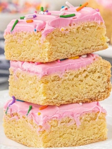 Stack of three cake mix Lofthouse sugar cookie bars topped with pink buttercream frosting and rainbow jimmies, showing the thick, dense, chewy texture.