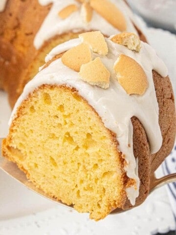 A close-up of a slice of Vanilla Wafer Bundt Cake with vanilla glaze and crushed vanilla wafers is served on a cake server, showing the moist, tender crumb.