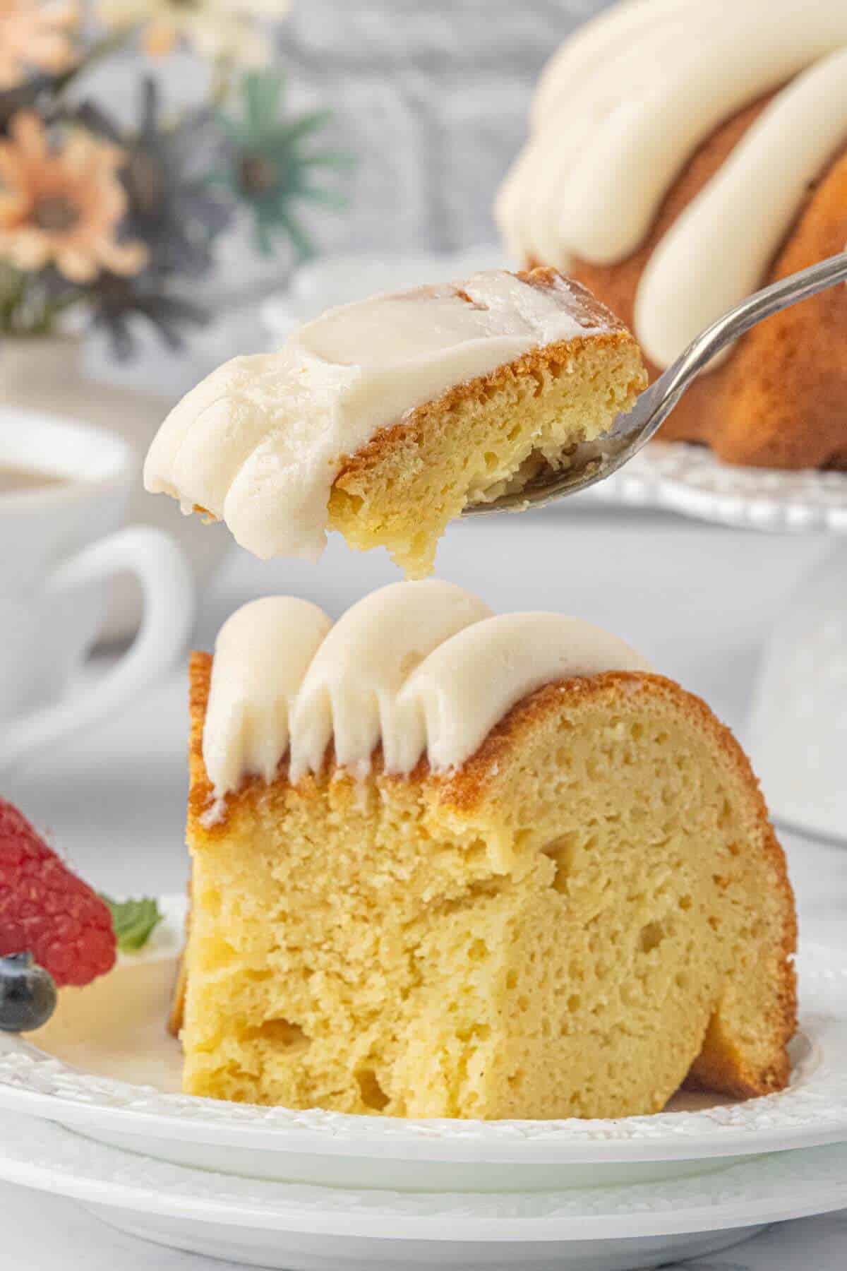 Forkful of tender vanilla cake and cream cheese frosting above a plated slice.