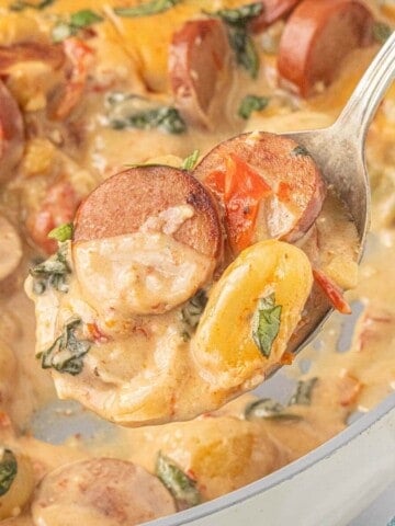 Spoonful of creamy potato gnocchi with browned chicken sausage, spinach and sun-dried tomatoes.
