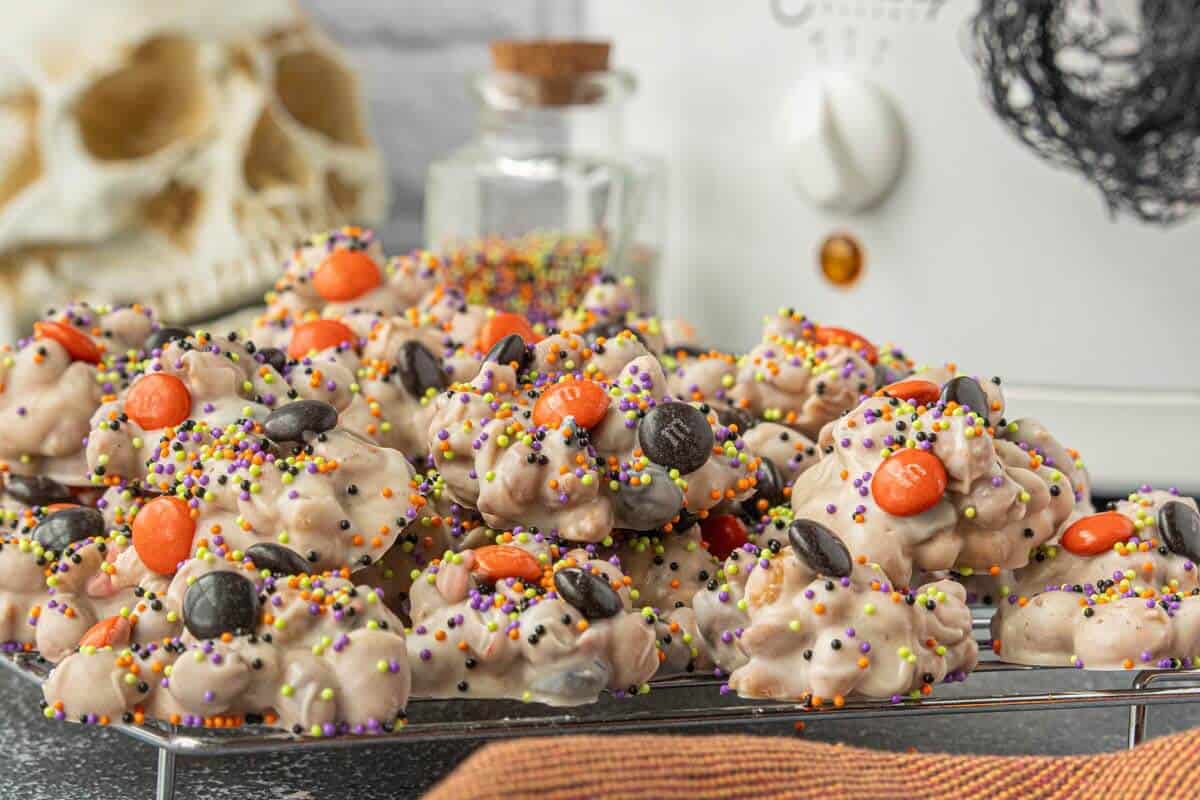 Creepy crockpot candy topped with orange and black M&M’s and colorful sprinkles on a cooling rack.