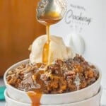 Crockpot Pumpkin Dump Cake with vanilla ice cream, chopped pecans and caramel sauce being drizzled over the top.
