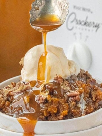 Crockpot Pumpkin Dump Cake with vanilla ice cream, chopped pecans and caramel sauce being drizzled over the top.