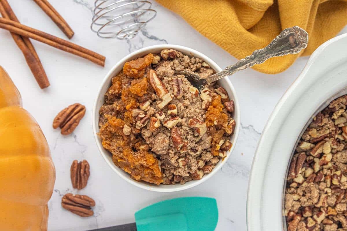 Bowl of Crockpot Pumpkin Dump Cake topped with buttery cake crumbles and chopped pecans.