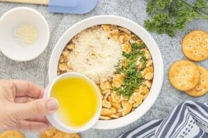 Melted butter being added to crushed Ritz crackers, Parmesan cheese, and fresh parsley for the casserole topping.