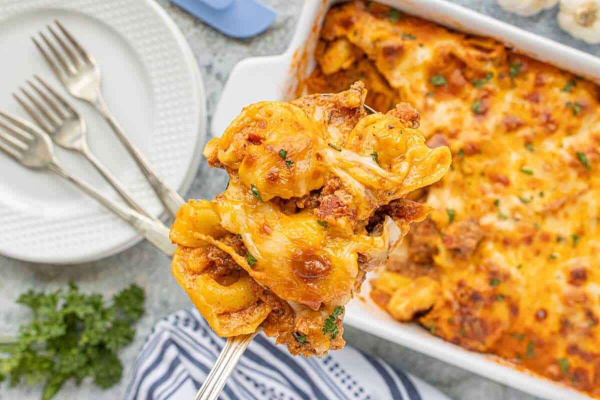 Serving of ground beef tortellini casserole in a serving spoon held above the casserole dish.