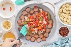 Frozen peppers and onions added to browned chicken sausage in the skillet.