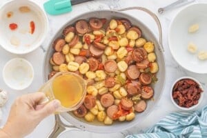 Chicken sausage, potato gnocchi and vegetables in a skillet as chicken broth is added.