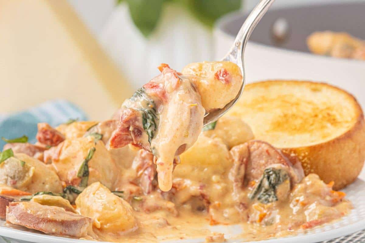 Forkful of creamy potato gnocchi with spinach and sun-dried tomatoes served with toasted bread.