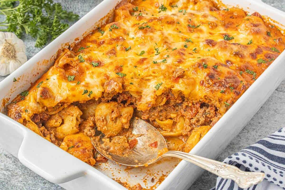 Ground beef tortellini casserole baked with golden melted cheese and parsley in a white casserole dish.