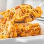 Spoonful of cheesy ground beef tortellini casserole lifted from the baking dish with melted cheese stretching from the spoon.