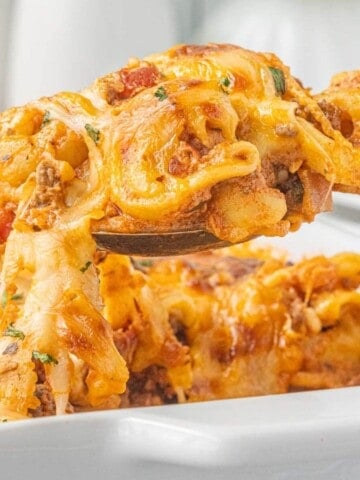 Spoonful of cheesy ground beef tortellini casserole lifted from the baking dish with melted cheese stretching from the spoon.