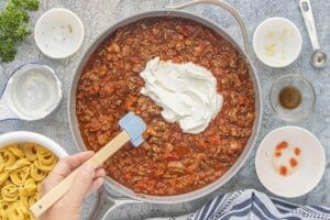 Sour cream being added to the ground beef and tomato sauce mixture in a large skillet.