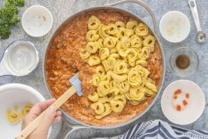 Cooked cheese tortellini being added to the creamy ground beef and tomato sauce.