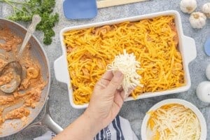 Shredded mozzarella being sprinkled over the tortellini casserole before baking.