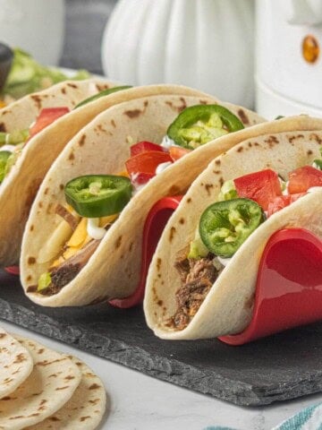Shredded beef tacos in soft flour tortillas topped with cheese, lettuce, tomatoes, jalapeños and sour cream.