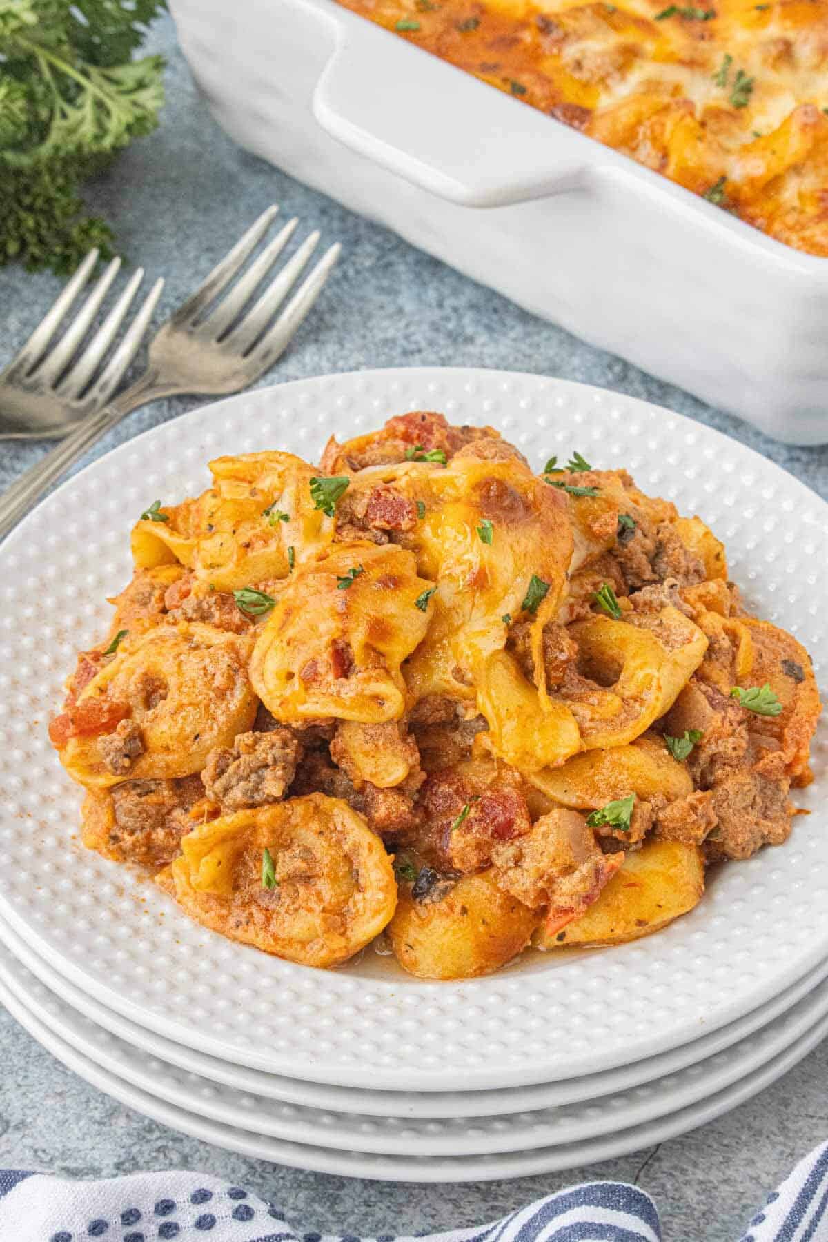 Ground beef and cheese tortellini casserole served on a white plate and garnished with fresh parsley.