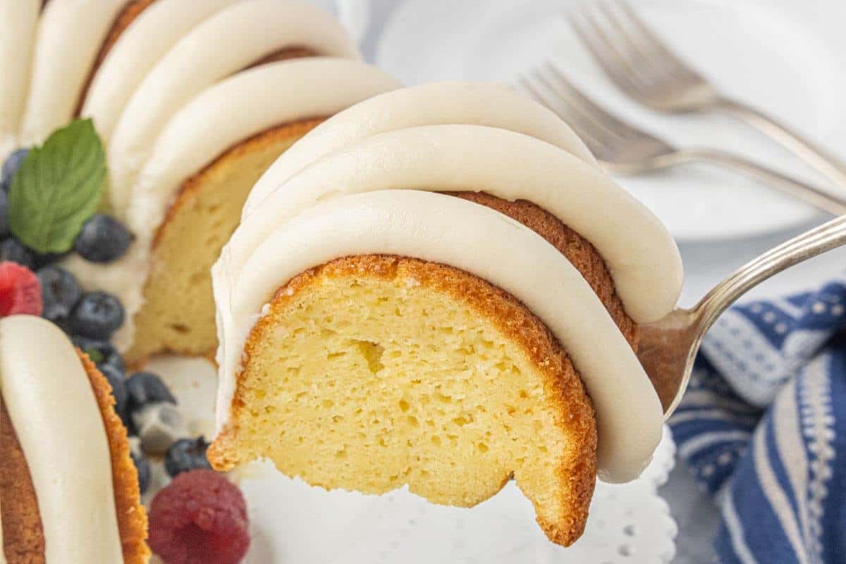 Thick slice of vanilla Bundt cake topped with ribbons of cream cheese frosting and served with fresh berries.