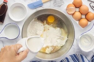 Pouring milk into a mixing bowl with cake mix, eggs, sour cream and other ingredients.
