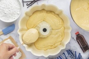 Spoonfuls of thick vanilla cake batter being added to a prepared Bundt pan.