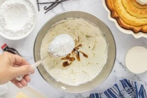 Adding powdered sugar and vanilla to the whipped cream cheese and butter mixture.