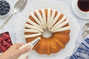 Piping thick ribbons of cream cheese frosting over the top and sides of the cooled Bundt cake.