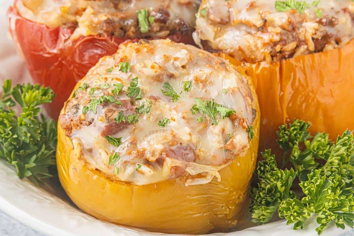 Close-up of a platter of stuffed bell pepper filled with ground beef, rice, tomato sauce, and melted mozzarella cheese, garnished with fresh parsley.