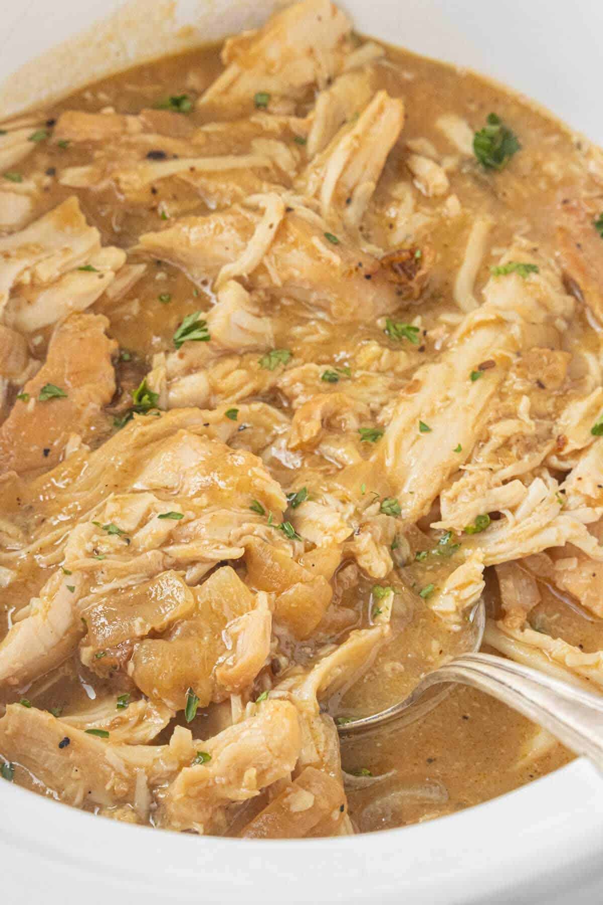 Close-up of shredded turkey mixed with savory brown gravy and garnished with fresh parsley in a crockpot with a serving spoon.
