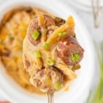 Close-up of a forkful of Crockpot Kielbasa and Potatoes garnished with fresh green onions.