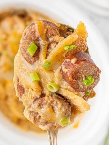 Close-up of a forkful of Crockpot Kielbasa and Potatoes garnished with fresh green onions.