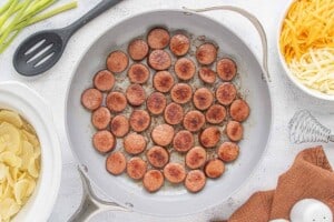 Sliced kielbasa browning in a large skillet until golden brown on both sides.