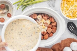 Creamy seasoned sauce being poured over kielbasa and potatoes in the crockpot.