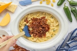 Adding crispy crumbled bacon to creamy Crockpot Bacon Jalapeño Mac and Cheese with tender pasta shells and melted cheese sauce.
