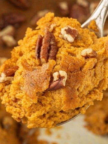 Close-up of a spoonful of spiced pumpkin dessert with golden brown edges and pecan pieces.