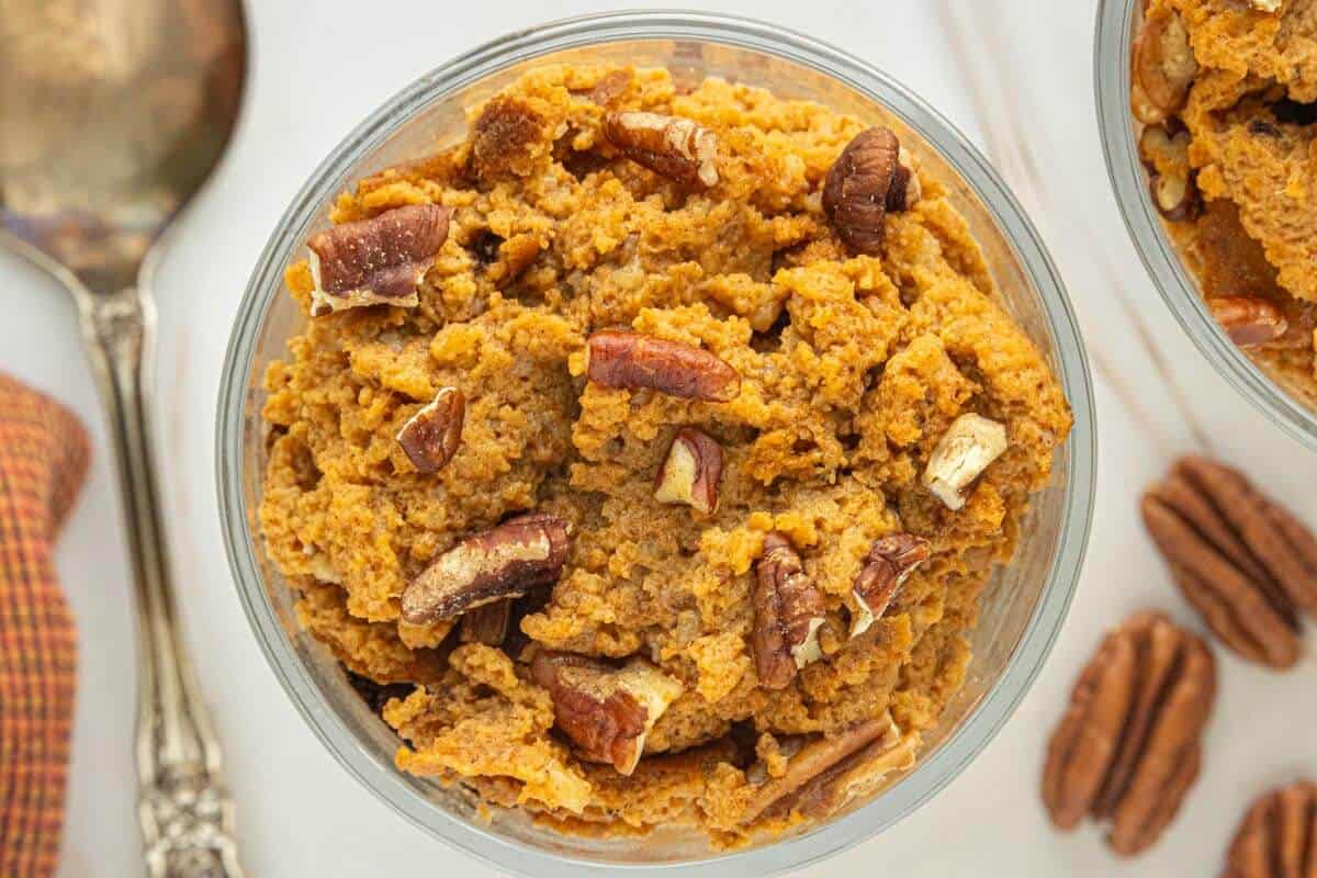 Overhead view of pumpkin pie pudding in a glass dessert bowl, topped with chopped toasted pecans.