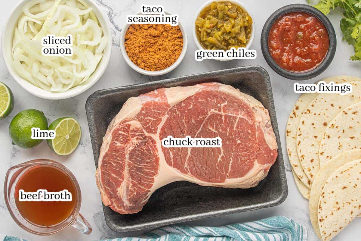 Ingredients for Crockpot Shredded Beef Tacos including chuck roast, sliced onion, taco seasoning, green chiles, beef broth, lime, tortillas and taco toppings.