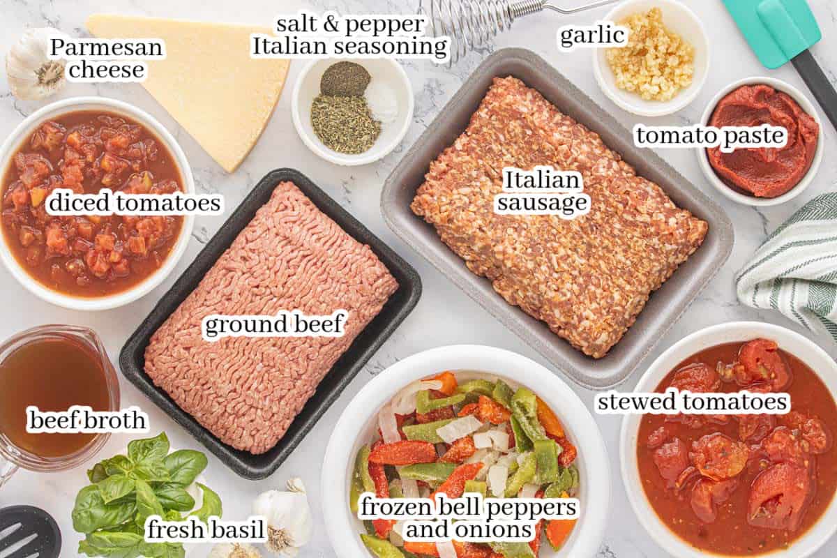 Overhead view of ground beef, Italian sausage, diced and stewed tomatoes, frozen peppers and onions, Parmesan cheese, garlic, herbs, and seasonings arranged on a marble countertop.