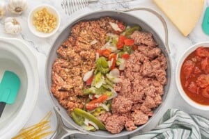Ground beef, Italian sausage, and frozen bell peppers and onions arranged in a large skillet before browning.