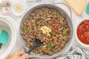 Browned ground meat mixed with saut&eacute;ed peppers and onions in a skillet, with minced garlic added on top.